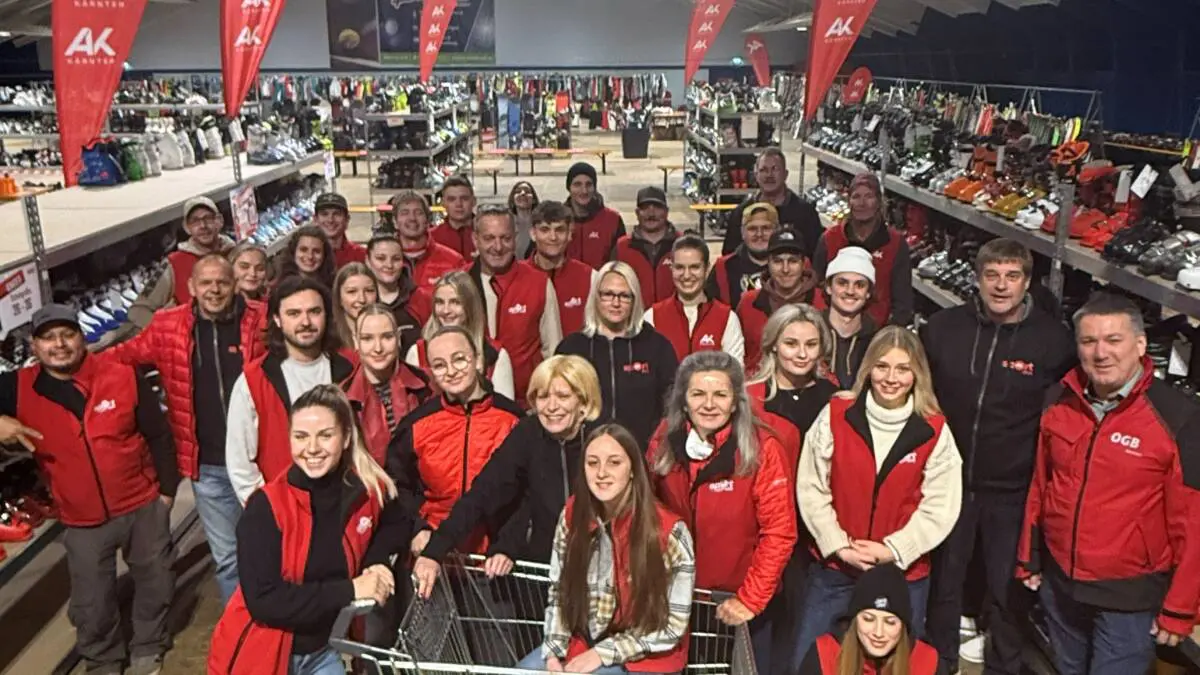Ein Team steht zwischen Wintersportartikeln und AK-Kärnten-Fahnen in einer Verkaufshalle.