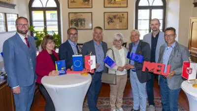 Teilnehmende stehen mit EU-Fahnen und einem roten EU-Schriftzug im Veranstaltungsraum.