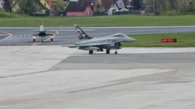 Eurofighter rollen über ein Flughafenvorfeld vor einer grünen Wiese.
