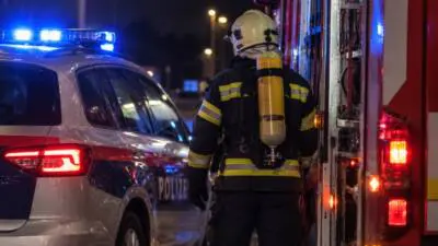Feuerwehrmann mit Atemschutz zwischen Polizeiauto und Löschfahrzeug bei Nacht