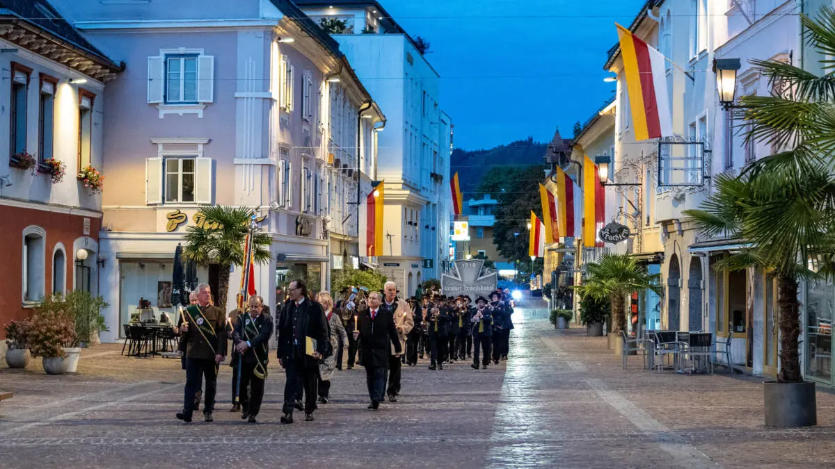 Ein Fackelzug zieht unter Fahnen durch eine abendlich beleuchtete Straße.
