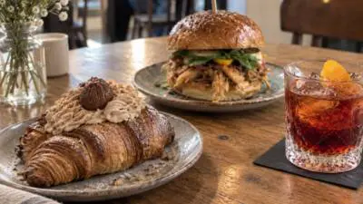 Maroni-Creme-Croissant und Burger auf Tellern neben einem Cocktail