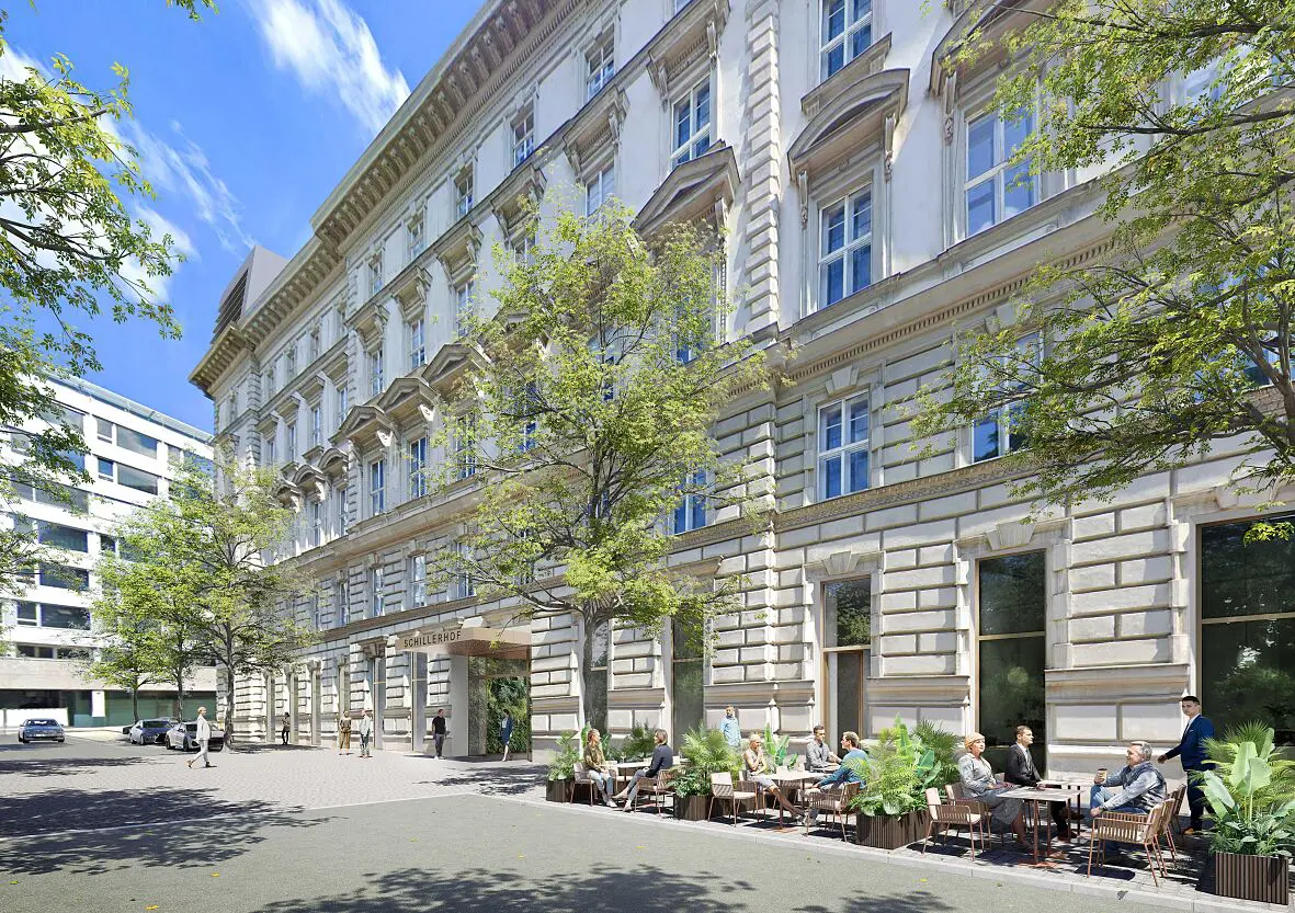 Die helle historische Fassade des Schillerhofs mit Gastgarten und Passanten in Wien.