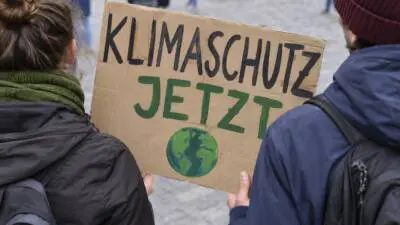Zwei Personen halten ein handgemaltes Klimaschutz-Schild mit Erdkugel auf einem Platz.