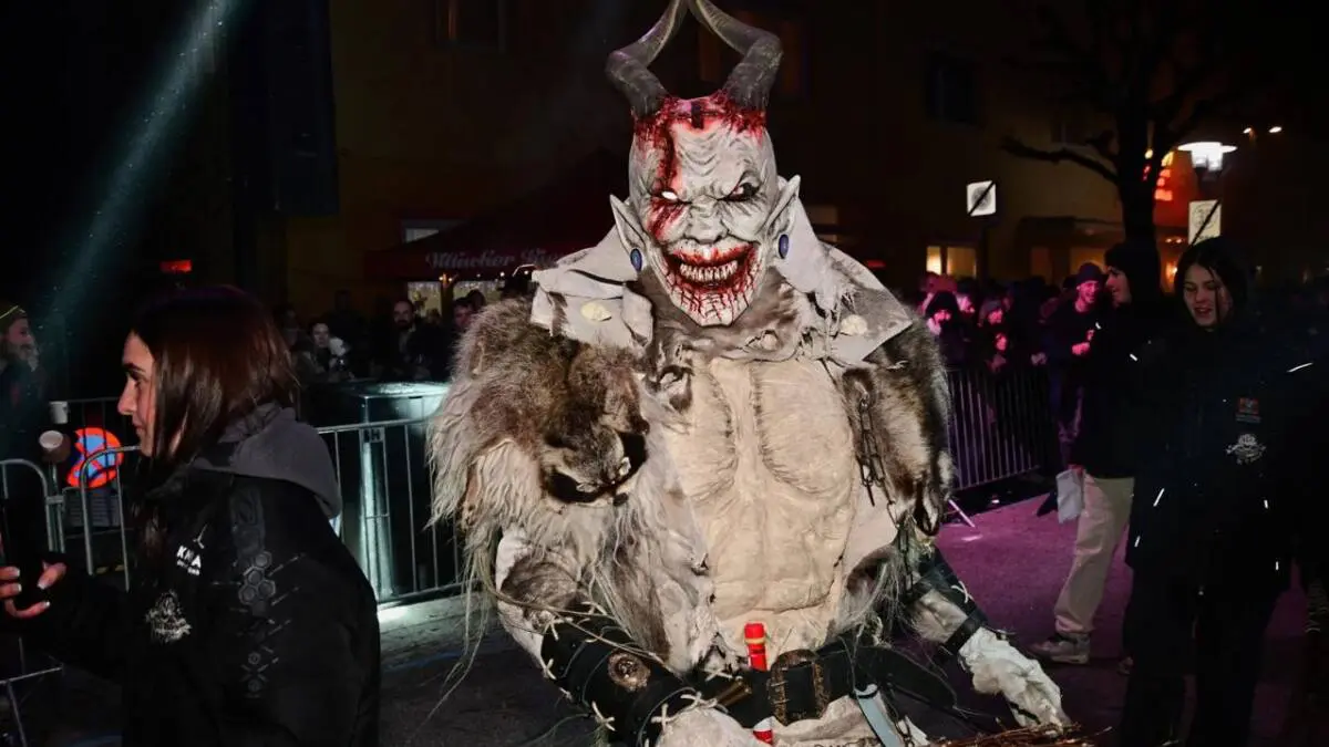 Eine Krampusfigur mit Hörnern und Fellkostüm steht bei einer nächtlichen Veranstaltung.