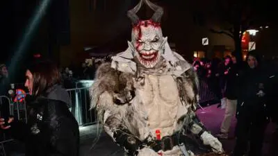 Eine Krampusfigur mit Hörnern und Fellkostüm steht bei einer nächtlichen Veranstaltung.