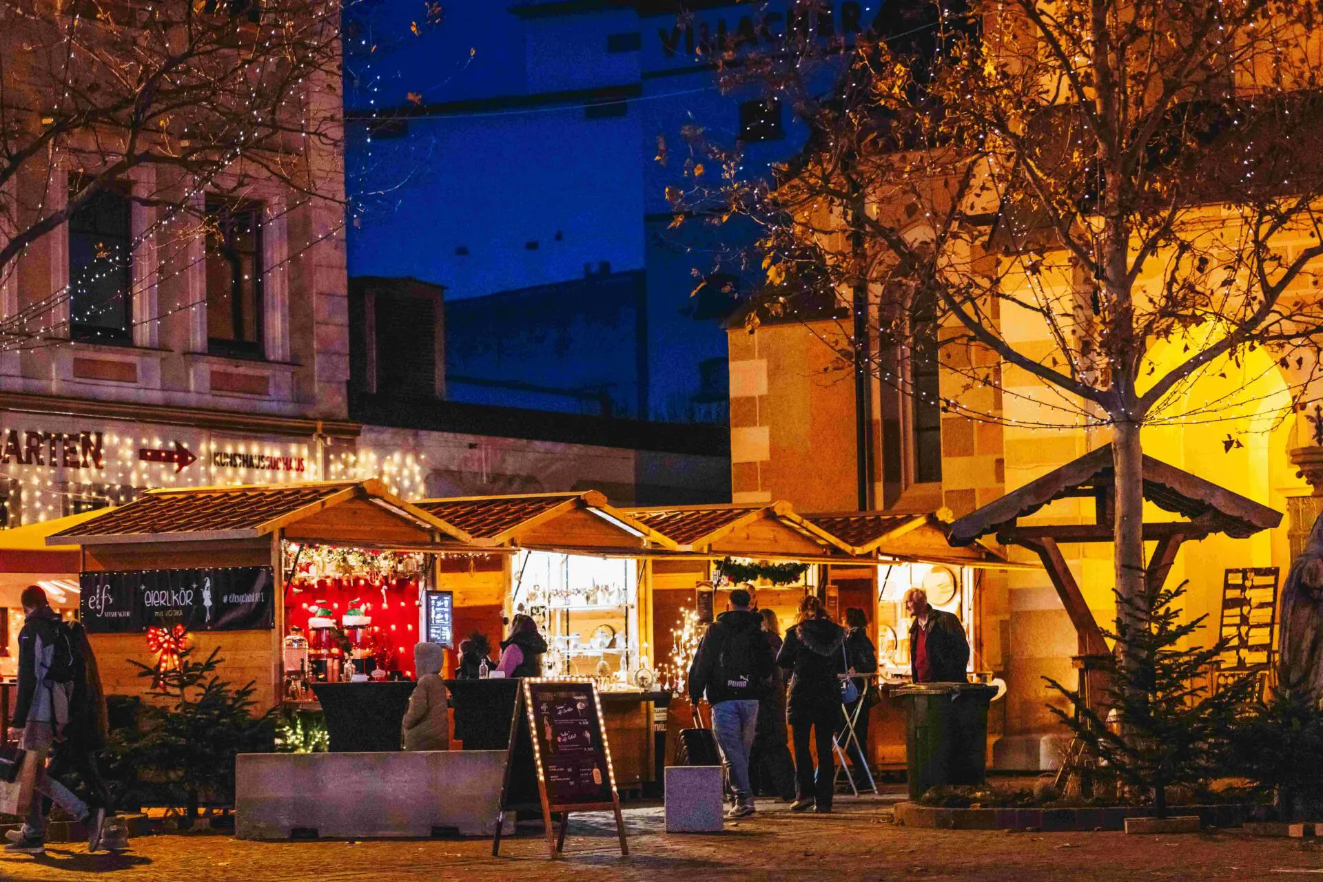 Beleuchtete Marktstände und Besucher auf einem Weihnachtsmarkt bei Nacht