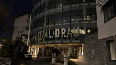 KI-generiertes Bild: Ein beleuchteter Krankenhauseingang mit verglaster Fassade bei Nacht.
