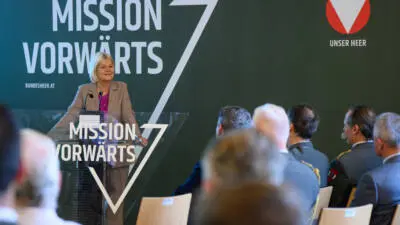 Klaudia Tanner spricht am Rednerpult vor sitzenden Gästen, darunter uniformierte Personen.