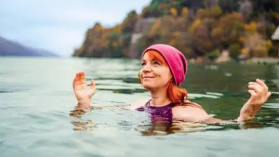 Eine Frau mit pinker Haube steht im Wasser und hebt die Hände.