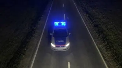 Ein weiß-blaues Polizeiauto mit blauem Blaulicht auf einer dunklen Landstraße