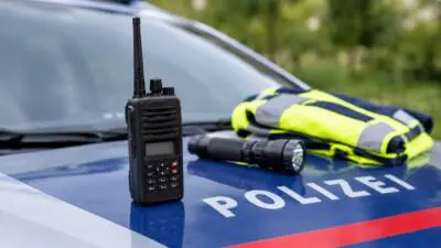 Funkgerät, Taschenlampe und Warnweste liegen auf der Motorhaube eines Polizeiautos.