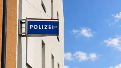 Blaues Polizeischild an heller Gebäudefassade vor blauem Himmel