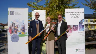 Drei Personen präsentieren bunte Kabel vor Bannern zur Breitbandstrategie Steiermark 2030.
