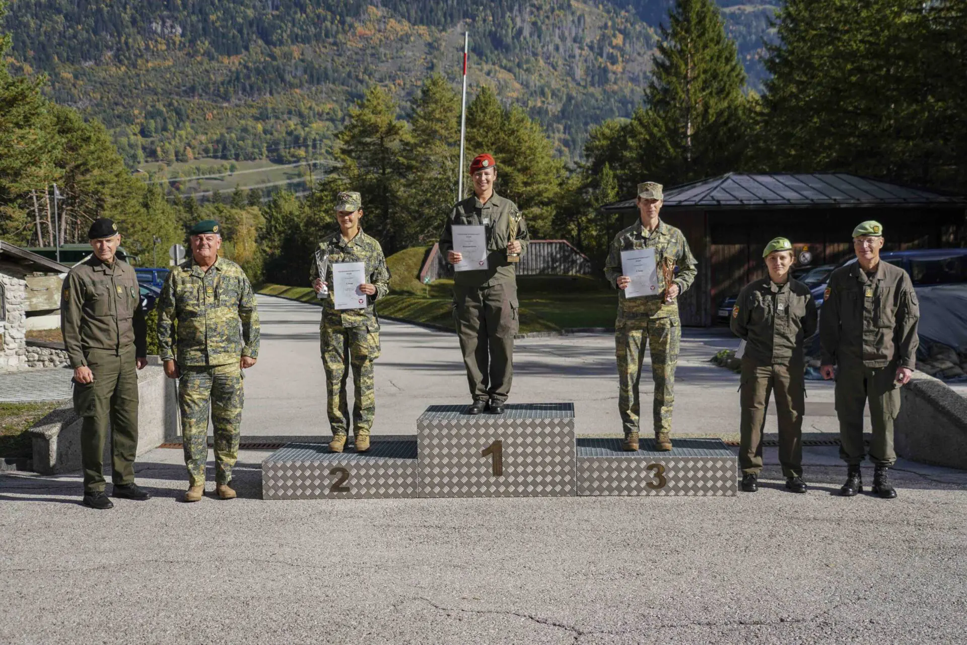 Soldatinnen und Soldaten stehen mit Urkunden und Pokalen auf einem Siegerpodest.