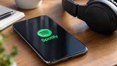 KI-generiertes Bild: Ein Smartphone mit Spotify-Logo liegt neben Kopfhörern auf einem Holztisch. Spotify prüft Familienabos nun auch per QR-Code.