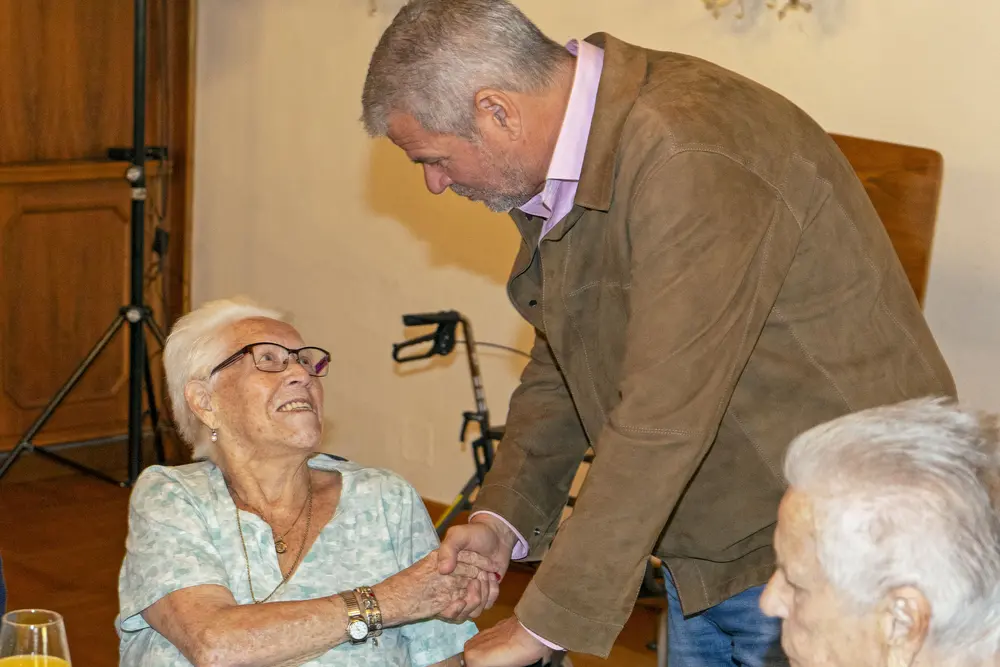 Ein Mann beugt sich zu einer älteren Frau und schüttelt ihre Hand.