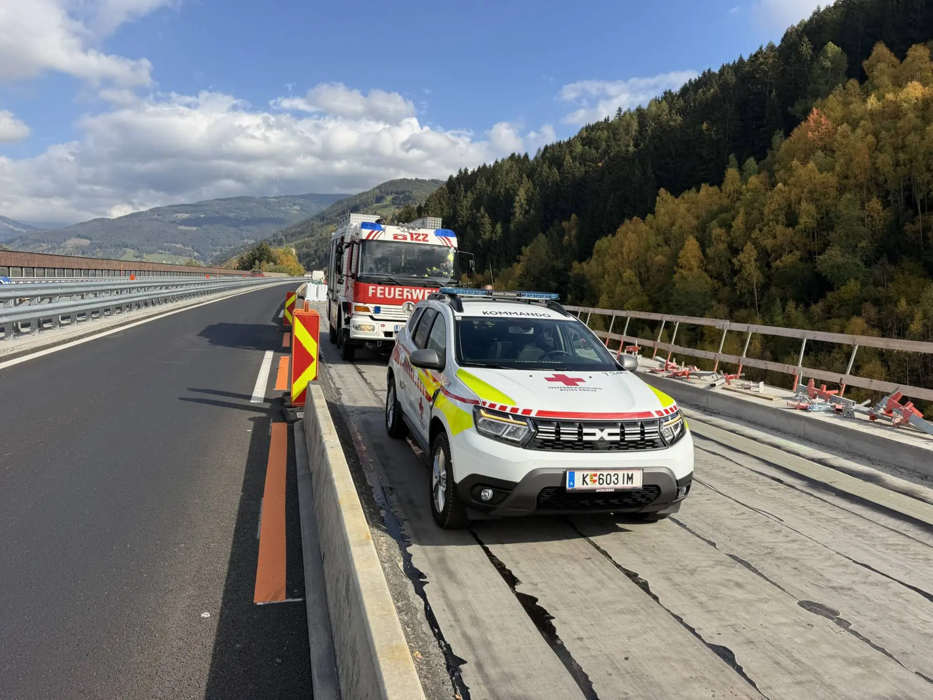 Feuerwehrfahrzeug und Einsatzwagen stehen auf einer durch Baustellenabsperrungen verengten Autobahnfahrbahn.