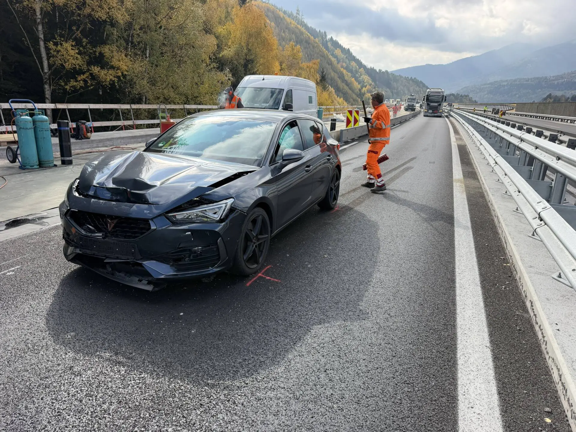 Dunkelgrauer Pkw mit beschädigter Front auf einer Baustellenfahrbahn