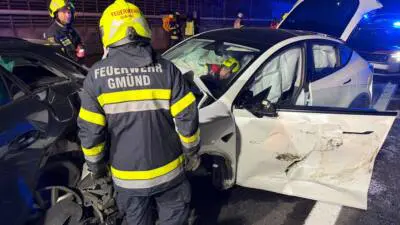 Feuerwehrleute neben beschädigten Autos, eine Fahrzeugtür ist geöffnet.
