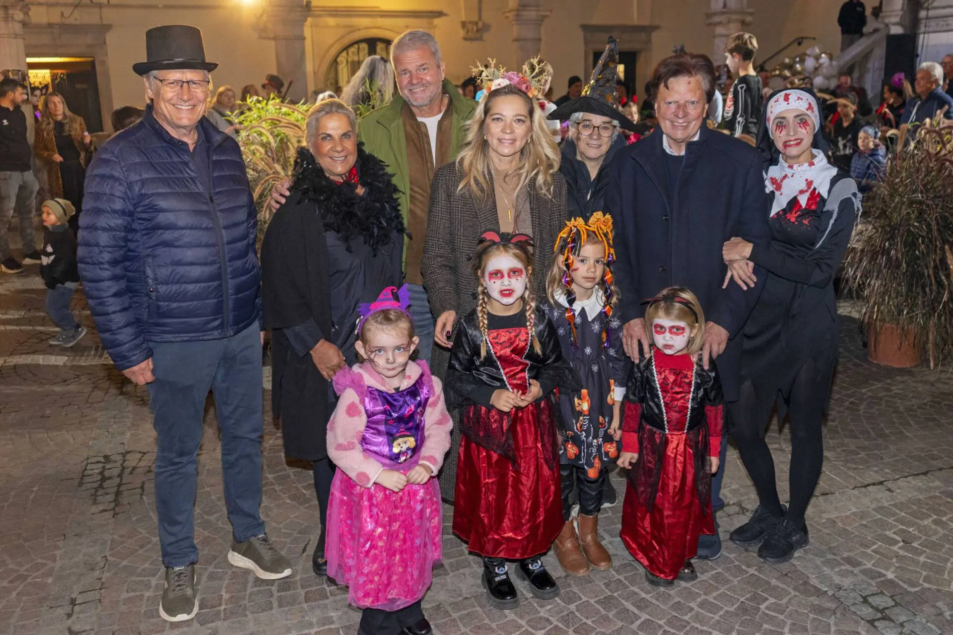 Erwachsene und kostümierte Kinder posieren bei einer abendlichen Veranstaltung in einem beleuchteten Innenhof.