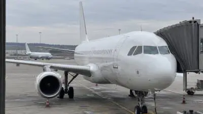 Weißes Passagierflugzeug steht auf einem Vorfeld neben einer Fluggastbrücke.