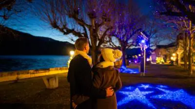 Ein Paar betrachtet blaue Lichtinstallationen am Ufer des Millstätter Sees.