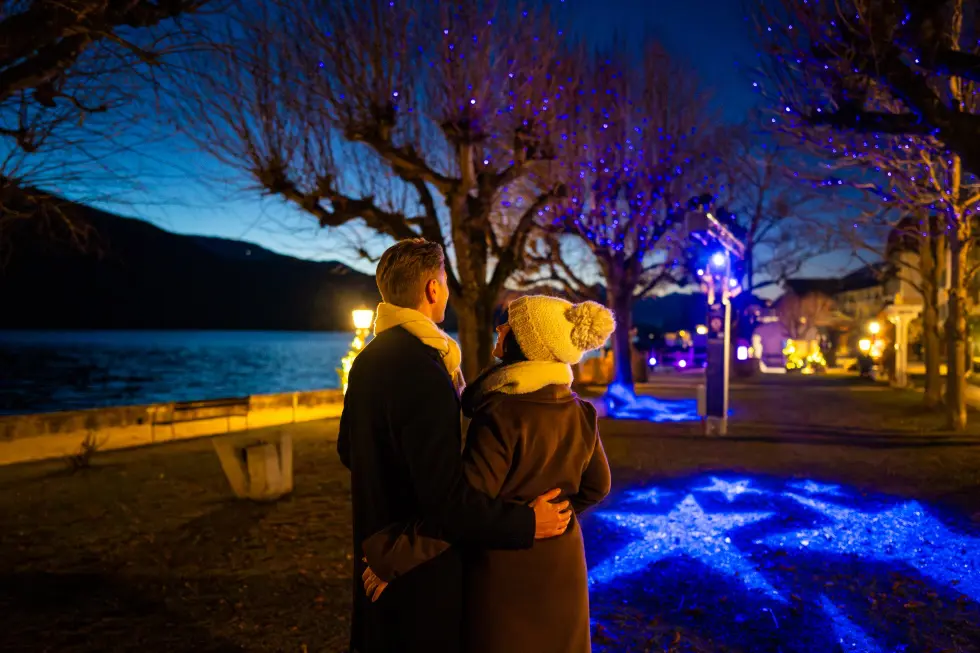 Ein Paar betrachtet blaue Lichtinstallationen am Ufer des Millstätter Sees.