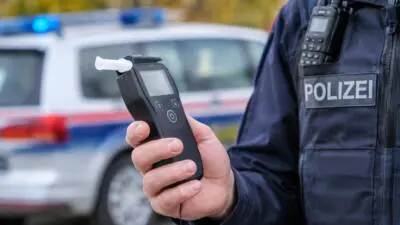 KI-generiertes Bild: Eine Person in Polizeiuniform hält ein Atemalkoholmessgerät vor einem Streifenwagen.