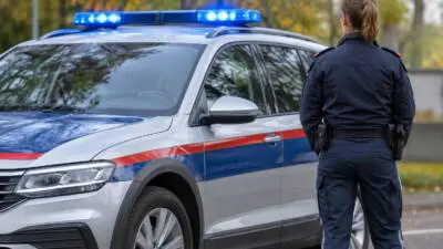 KI-Symbolbild: Eine uniformierte Frau steht neben einem silbernen SUV mit blauem Lichtbalken.