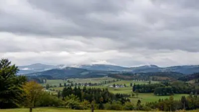 KI-Symbolbild: Dichte Wolken über einer grünen Hügellandschaft.