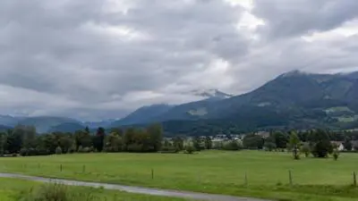 KI-Symbolbild: Graue Wolken ziehen über bewaldete Berge und ein grünes Tal.