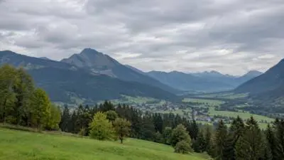KI-Symbolbild: Ein grünes Tal und Berge unter bewölktem Himmel.