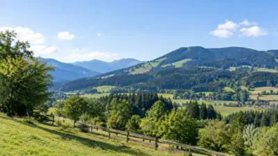 KI-Symbolbild: Eine sonnige Berglandschaft mit grünen Hängen unter blauem Himmel.