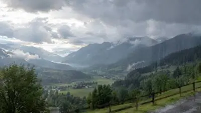 KI-generiertes Bild: Wolkenverhangene Berglandschaft mit grünen Hängen und einem Holzzaun im Vordergrund.
