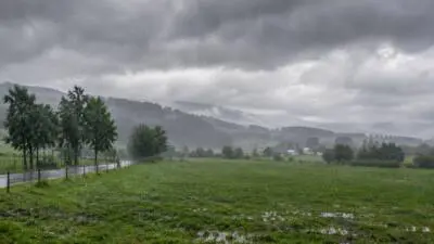KI-Symbolbild: Regen über grüner Landschaft mit einer Straße und bewaldeten Hügeln.