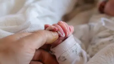 KI-Symbolbild: Eine kleine Hand umschließt den Finger einer erwachsenen Hand.