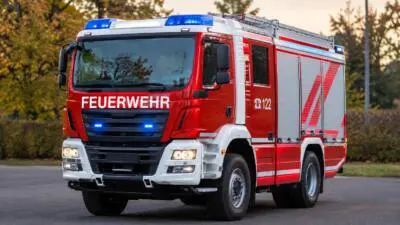 KI-Symbolbild: Ein rotes Feuerwehrfahrzeug mit Blaulicht steht auf einer Straße.