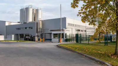 KI-Symbolbild: Ein graues Industriegebäude mit Silotanks hinter einem Werkszaun.