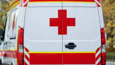 KI-Symbolbild: Heck eines weißen Rettungswagens mit rotem Kreuz und blauen Warnleuchten.