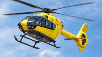 KI-Symbolbild: Ein gelber Hubschrauber fliegt vor blauem Himmel.
