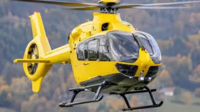 KI-Symbolbild: Ein gelber Hubschrauber vor bewaldeter Hügellandschaft.
