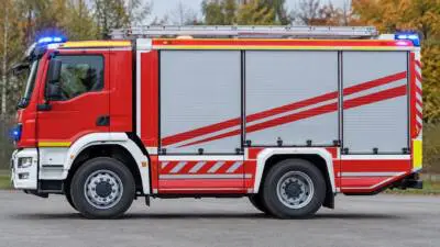 KI-generiertes Bild: Ein rotes Einsatzfahrzeug mit weißen Seitenfächern steht vor herbstlichen Bäumen.