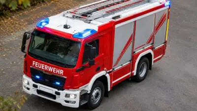 KI-Symbolbild: Ein rotes Feuerwehrfahrzeug mit eingeschaltetem Blaulicht steht auf einer Straße.