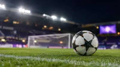 KI-generiertes Bild: Ein Fußball liegt auf dem Rasen vor einem beleuchteten Stadion.