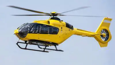 KI-Symbolbild: Ein gelber Hubschrauber fliegt vor hellem Himmel.