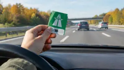KI-Symbolbild: Eine Hand hält eine grüne Karte mit Autobahnsymbol vor einer Autobahn.