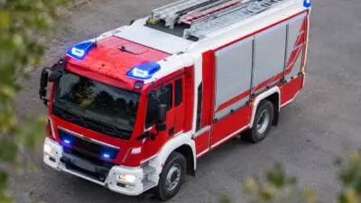 Roter und weißer Feuerwehr-Lkw mit Leitern und Blaulicht auf einem Schotterplatz