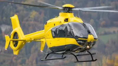 KI-generiertes Bild: Ein gelber Hubschrauber fliegt vor einer bewaldeten Berglandschaft.