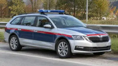 KI-Symbolbild: Ein silberner Kombi mit blau-roten Streifen und Blaulicht an einer Straße.